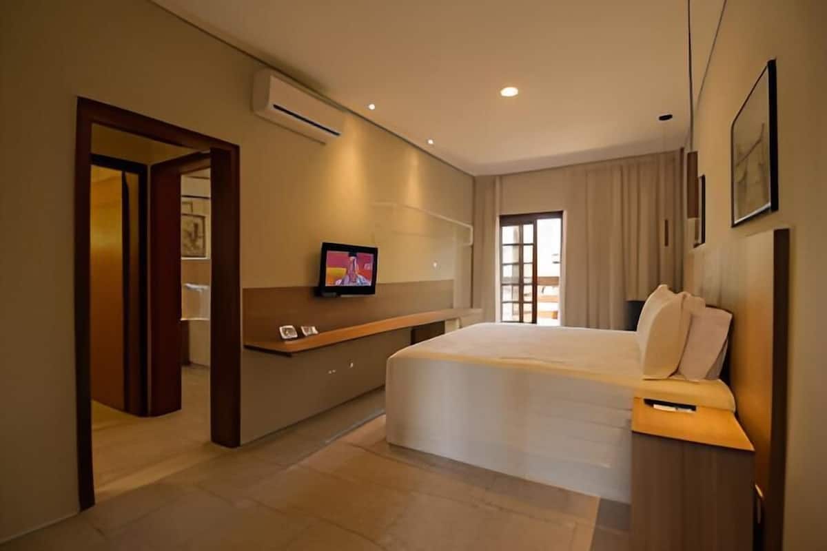 A modern hotel room with a large bed, a TV mounted on the wall, and a desk with a telephone.