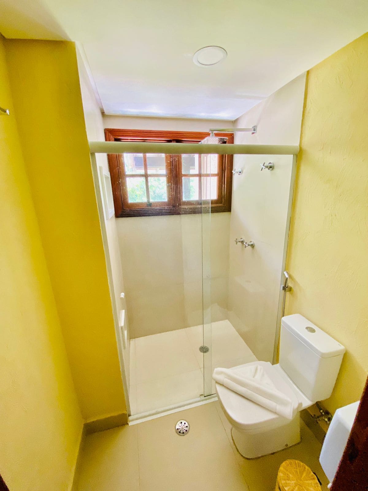 Une petite salle de bain avec une douche à parois de verre, des toilettes et une fenêtre avec des rideaux.