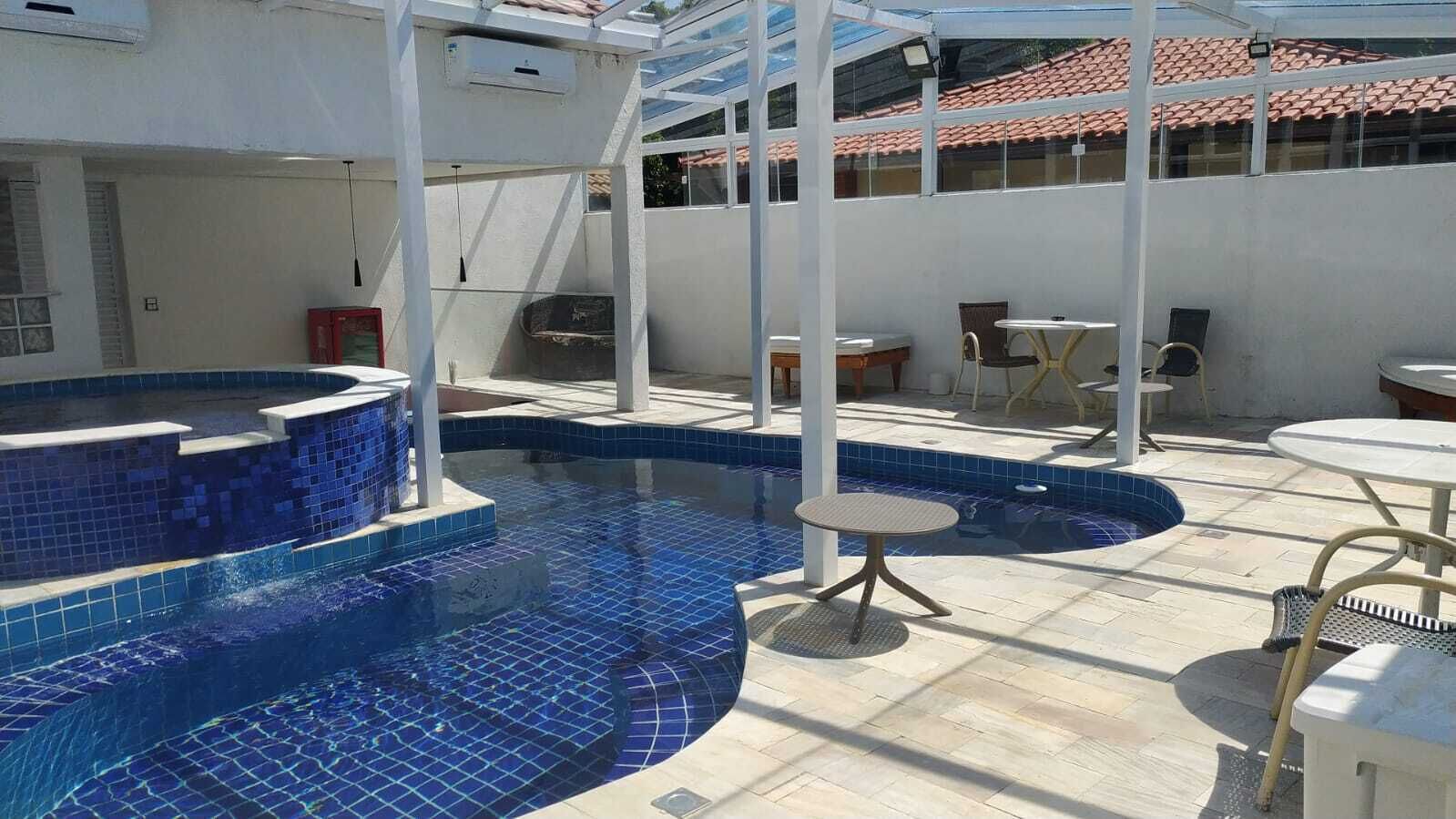 A rooftop swimming pool with blue tiles, surrounded by outdoor furniture and a covered area.