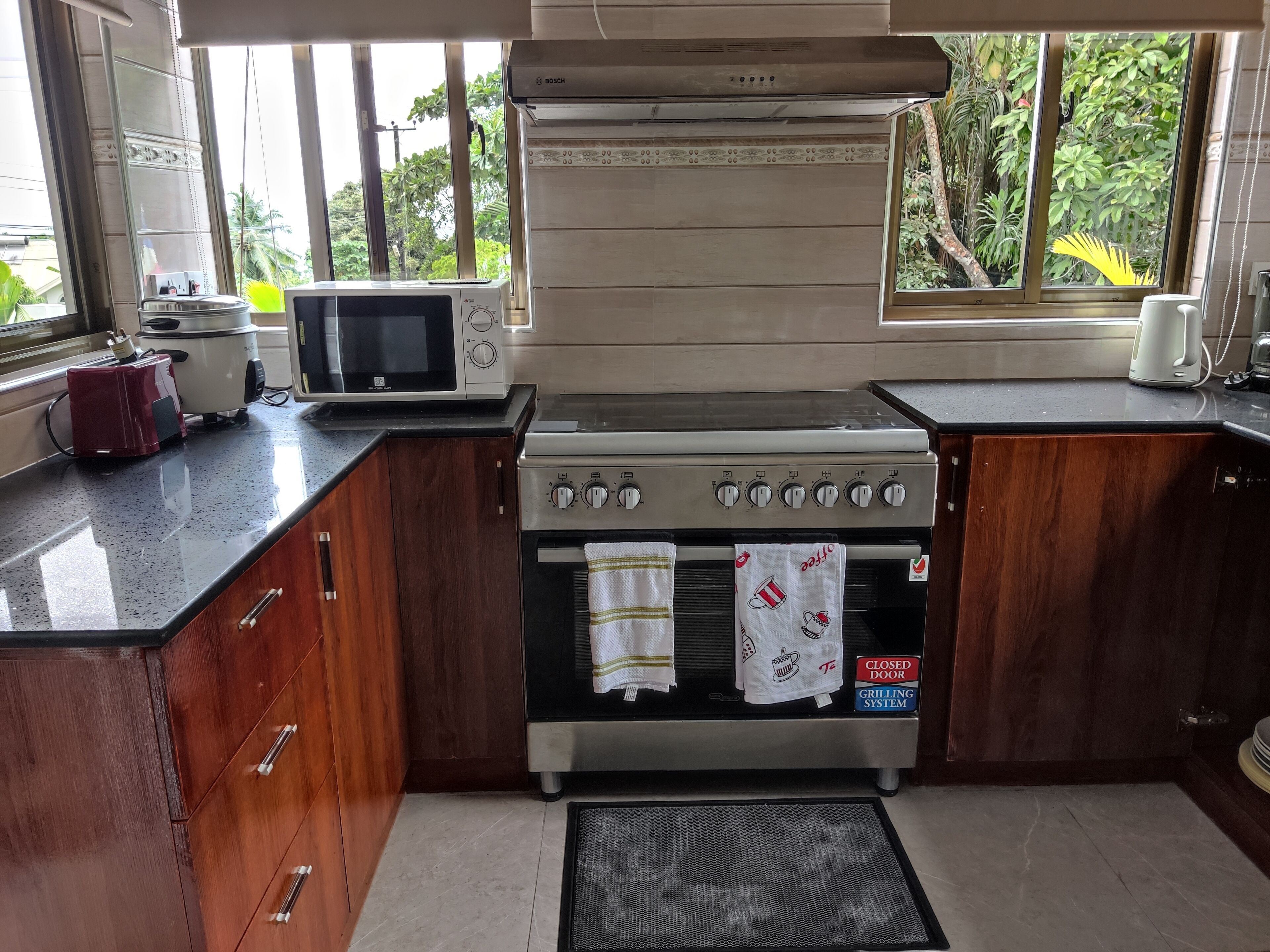 Una cocina con microondas Bosch, una tostadora roja, una estufa y un cartel que indica un sistema de parrilla.