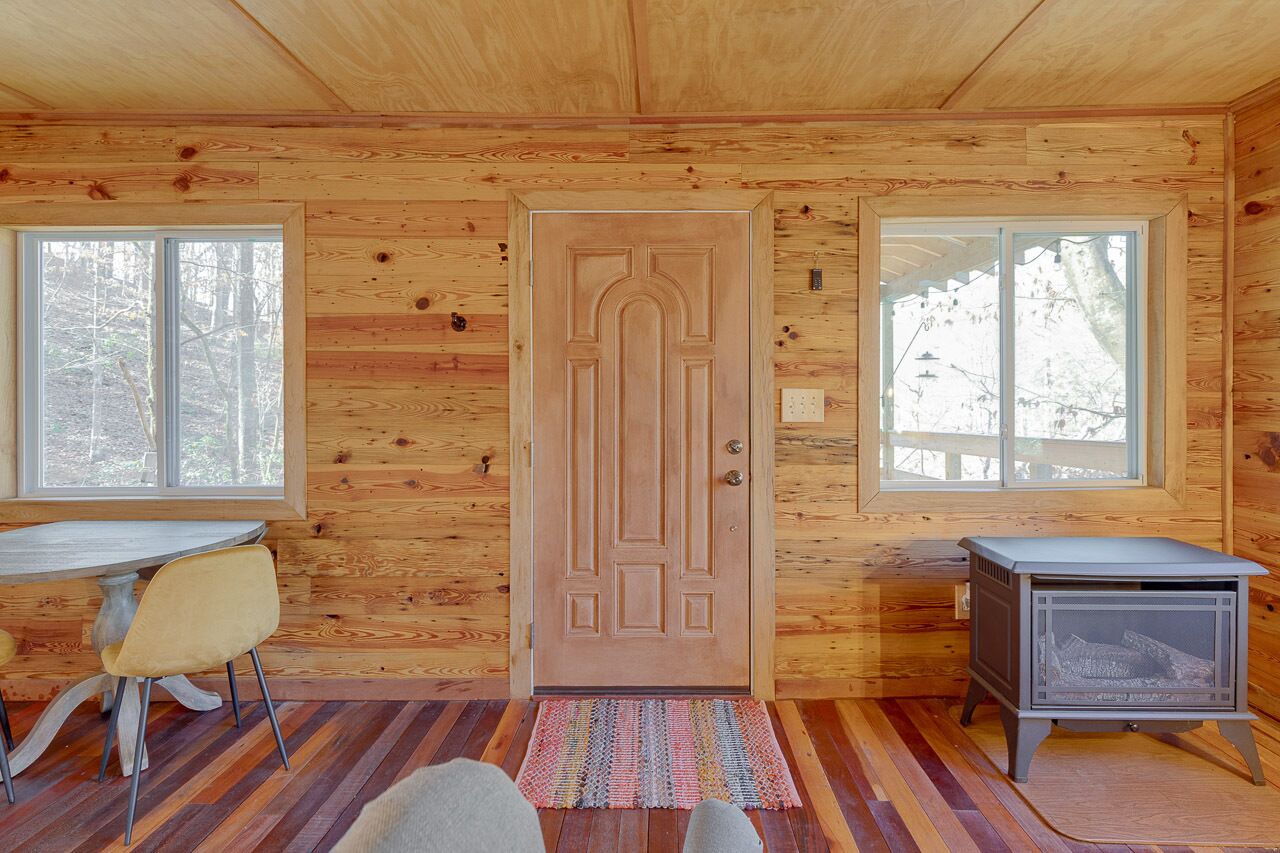L’intérieur d’un chalet en bois, avec une table à manger, deux chaises, une porte et un poêle à bois.