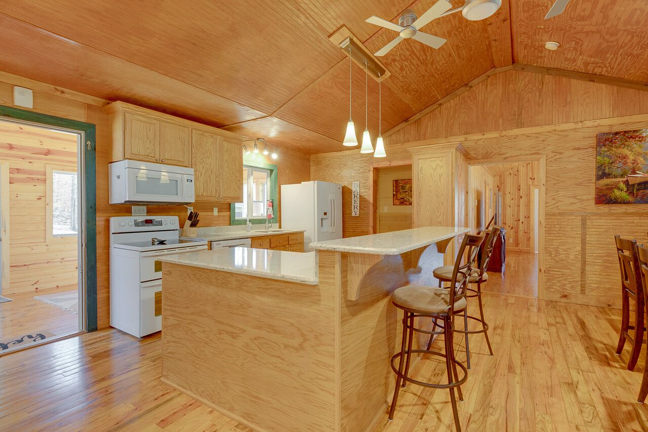 A wooden interior with a kitchen island, bar stools, and a ceiling fan.