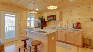 Interno di una baita in legno con una cucina che include un'isola grande, sgabelli da bar e mobili contenitori in legno.