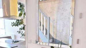 Un salon moderne avec un grand miroir, un meuble de rangement noir pour les appareils électroniques, une table à manger en bois et une plante en pot.