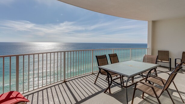 A balcony with a table and chairs, overlooking a clear view of the ocean.