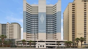 A high-rise hotel with a prominent logo, multiple balconies, and a parking garage.
