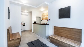 Un espace d’accueil comprenant un banc en bois, un comptoir de réception, une œuvre d’art accrochée au mur et une plante en pot.