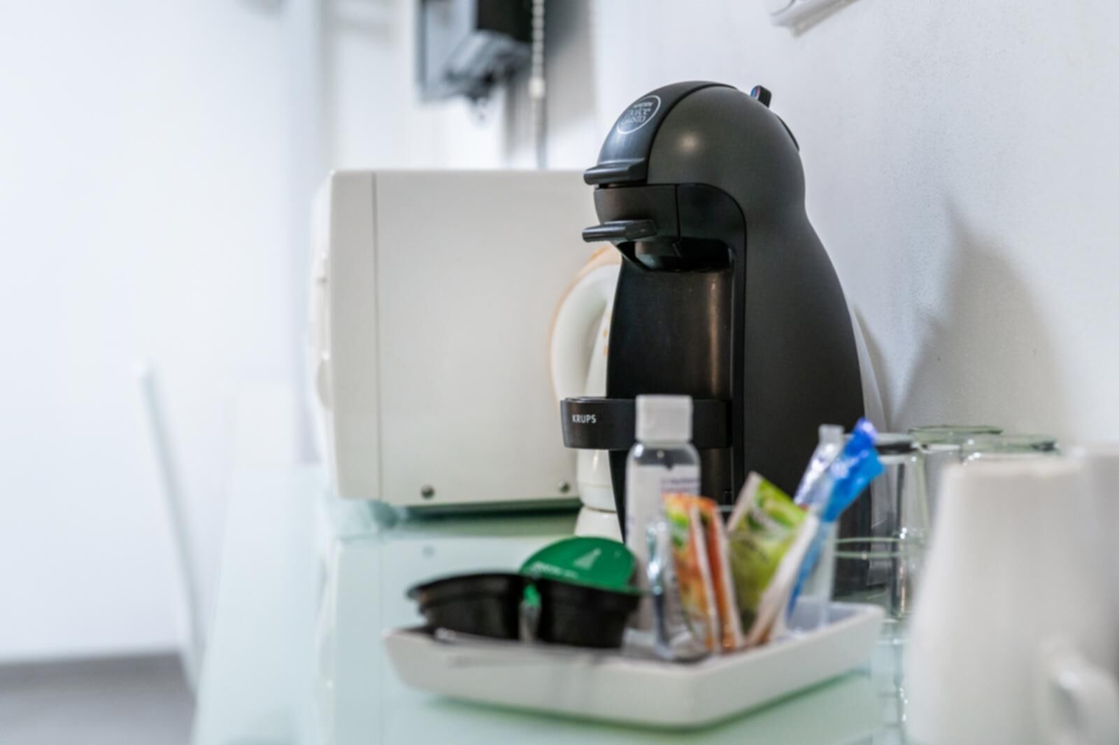 A coffee machine on a table with a tray containing a bottle, packets, and a cup.