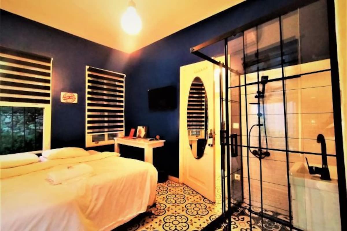 A room with a bed, a small table, a shower area, and a television.