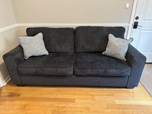 A dark grey sofa with two patterned throw pillows in a room with wooden flooring and a white door in the background. - The Garden Suite at Moon Lake Farm - come stay at the farm (Belden)