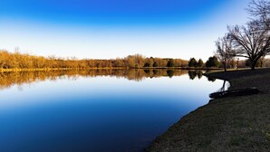 Un lac paisible aux eaux claires, dont la surface reflète parfaitement le paysage environnant, bordé d’arbres et entouré d’une zone herbeuse.