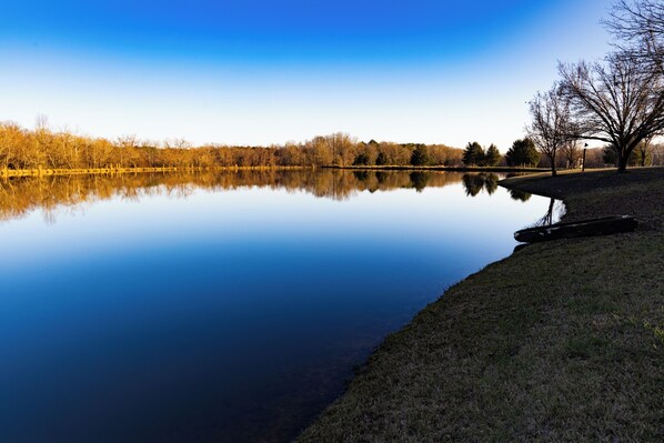 A calm lake with a clear reflection, surrounded by trees and a grassy area.