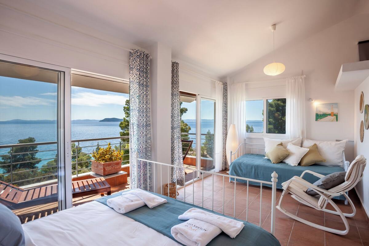 Un balcón con vista al mar, una cama con cabecera azul y una mecedora.