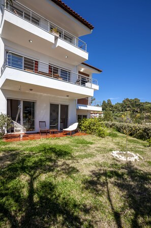 Une maison moderne à deux étages, dotée d’un balcon, d’une terrasse avec mobilier d’extérieur et offrant une vue sur le paysage environnant.