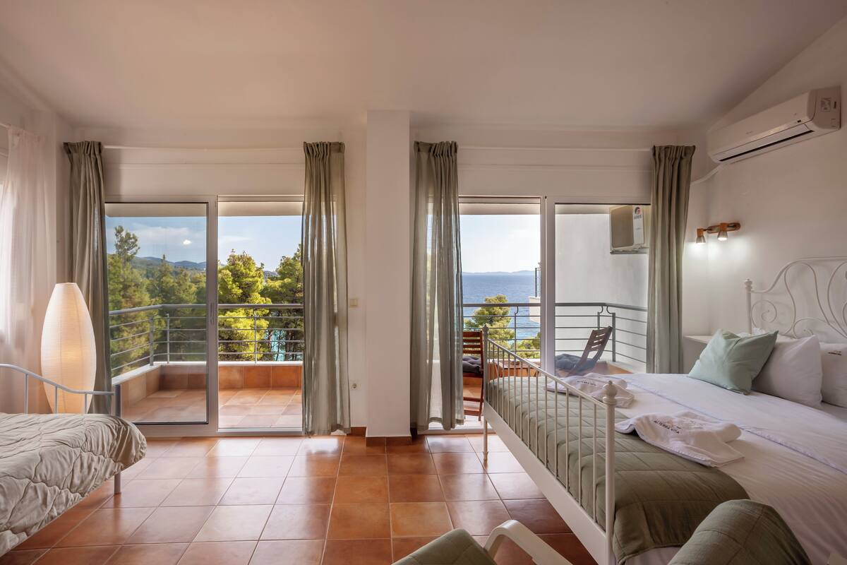 Un dormitorio con balcón, una cama, una silla y un ventanal grande con cortinas.
