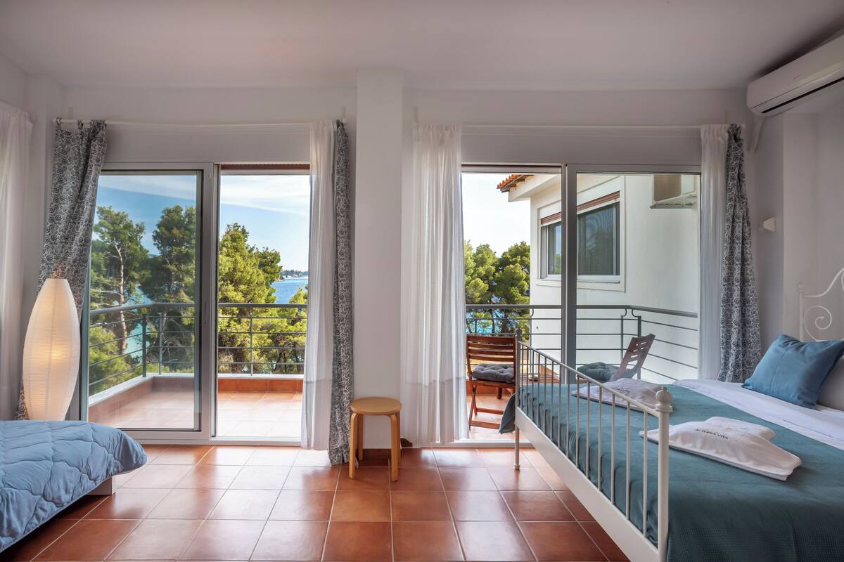 Un dormitorio moderno con balcón, una cama con colcha azul, una mesita y una silla.