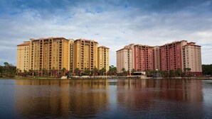 A large hotel with multiple high-rise buildings, a body of water in the foreground, and a clear sky.
