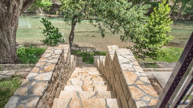 A stone staircase leading to a riverbank with trees and greenery.