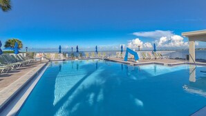 A swimming pool with lounge chairs and umbrellas, surrounded by a white fence and palm trees. - Luxury Waterfront Condo with Heated Pool and Balcony (Tampa)