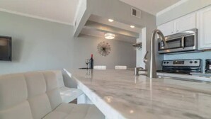 A modern kitchen with a marble countertop, stainless steel appliances, and a white sofa. - Luxury Waterfront Condo with Heated Pool and Balcony (Tampa)