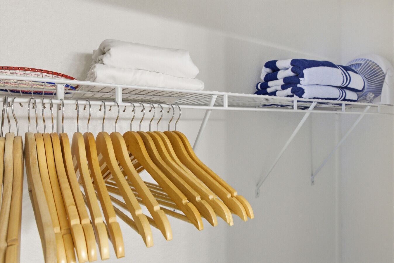 A white closet with wooden hangers and folded clothes.