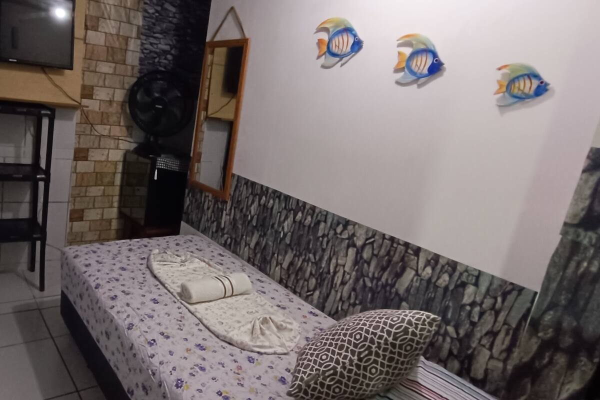A small bedroom with a bed, a desk, a TV, and decorative fish wall art.