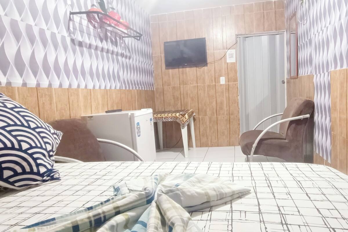 A hotel room with a bed, a desk, a chair, a TV mounted on the wall, and a shower area.