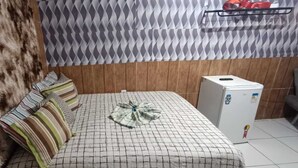 Un dormitorio con cama, almohadas estampadas, una manta de piel, cortina con diseño y un refrigerador blanco pequeño.