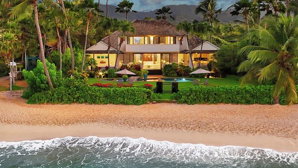 Une propriété située en bord de mer, comprenant une maison à deux étages, une piscine et une végétation luxuriante.