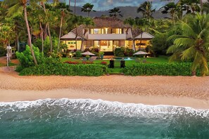 A beachfront property with a two-story house, a swimming pool, and lush greenery. - Waiohai Beach House: Poipu Beachfront Estate (Koloa)