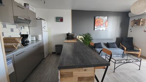 Une cuisine moderne avec un îlot central en bois, un coin repas avec un canapé et des chaises, et un espace de vie doté d’une grande fenêtre et d’œuvres d’art.