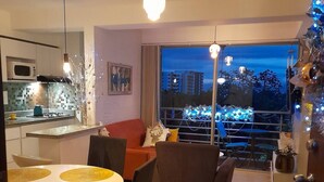 Un appartement moderne comprenant un coin repas, une cuisine et un balcon offrant une vue sur la ville.