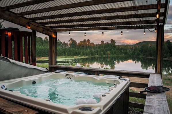 A hot tub under a wooden pergola with a view of a lake and forest.