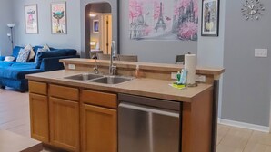 A modern kitchen with a central island, a dining area with a blue sofa, and a living room with a ceiling fan. - The Glenbrook Getaway – 4BR Resort Home with Pool & Spa (Four Corners)