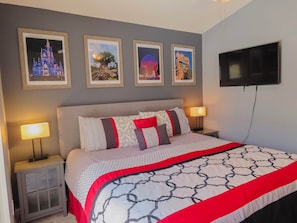 A neatly arranged hotel room with a bed, two bedside tables, a TV, and framed pictures on the wall.