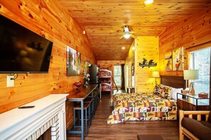 A log cabin interior with a bed, a dining area, and a TV mounted on the wall.
