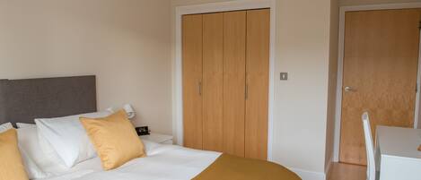 A bedroom with a bed, a wardrobe, and a desk with a chair.