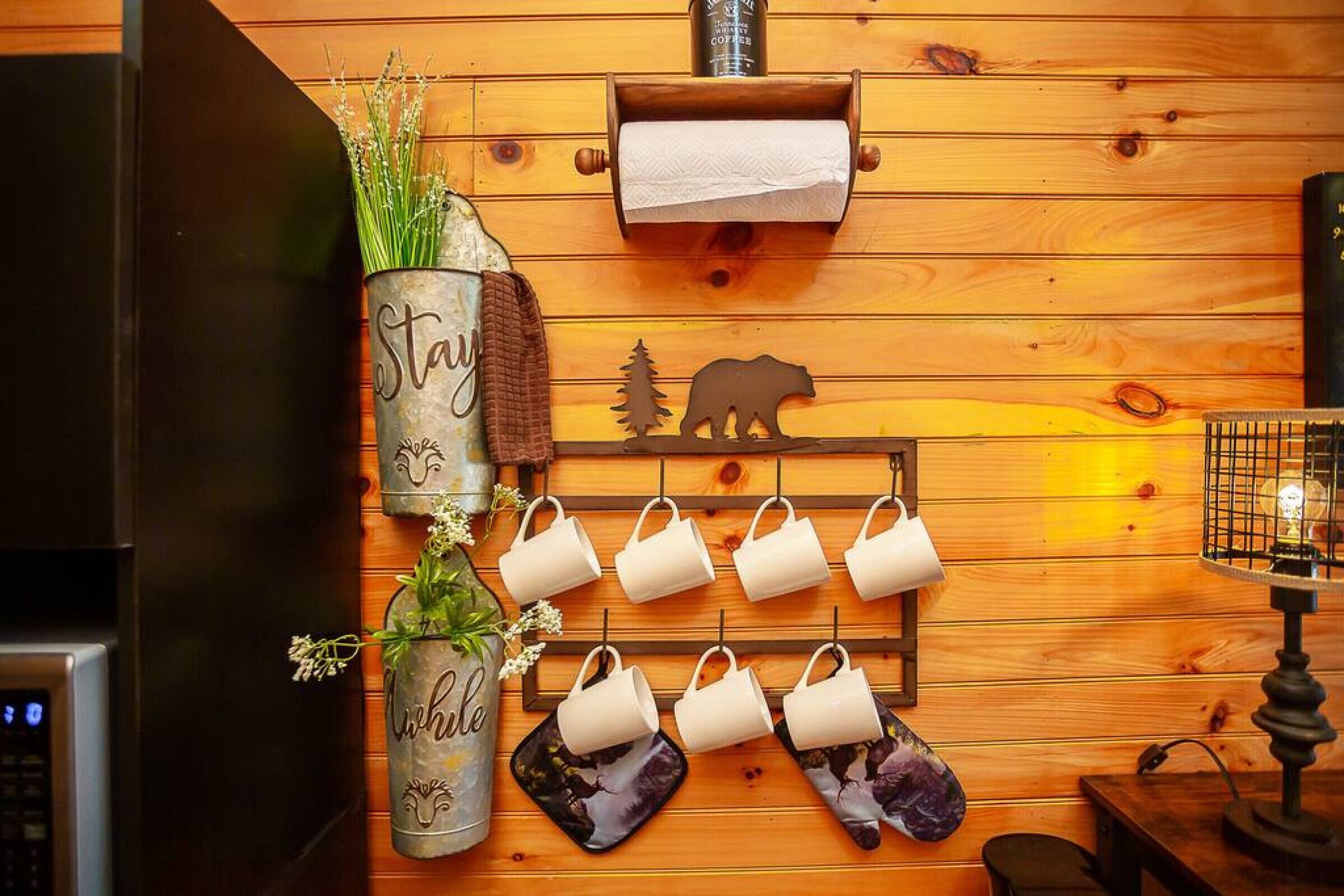 Une cuisine avec des murs en bois, une machine à café, un distributeur d’essuie-tout et une décoration représentant la silhouette d’un ours.