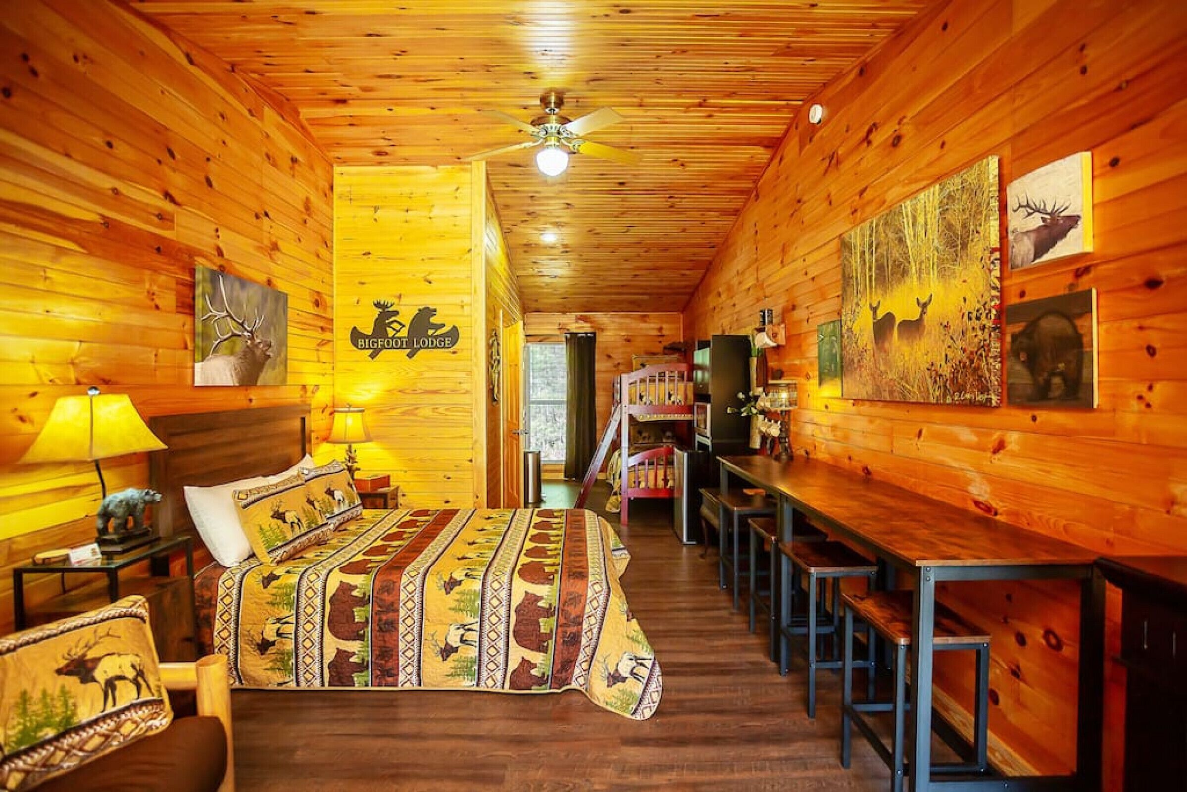 Habitación tipo cabaña de madera con cama, escritorio y sillas, paredes y techo de madera, y obras de arte con motivos de animales salvajes.