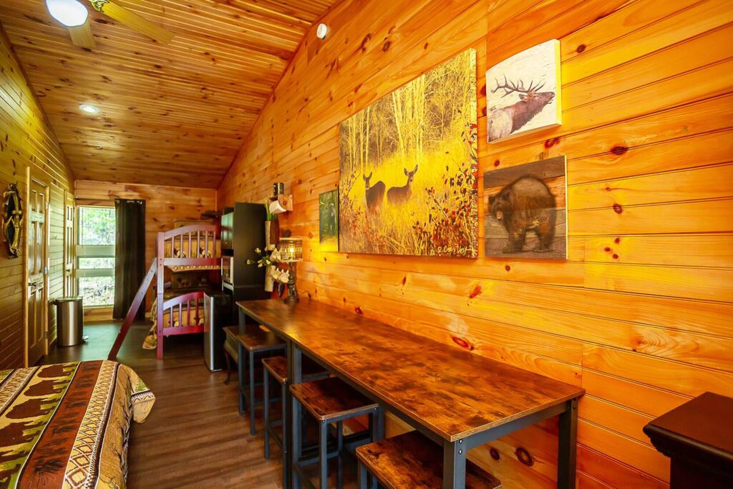 L’intérieur d’un chalet en bois, avec une longue table à manger, des bancs et des tableaux représentant des cerfs et des élans, accrochés aux murs.