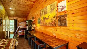 L’intérieur d’un chalet en bois, avec une longue table à manger, des bancs et des tableaux représentant des cerfs et des élans, accrochés aux murs.