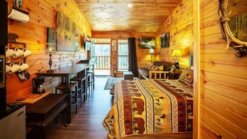 L’intérieur d’un chalet confortable, avec des murs en bois, une table à manger en bois, des bancs, un canapé et un lit recouvert d’une couverture à motifs.