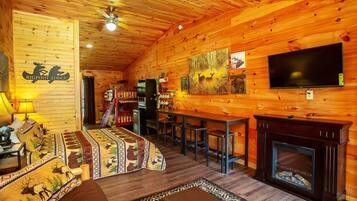 Un intérieur chaleureux et accueillant, avec des murs en bois, une cheminée, un téléviseur et un coin repas.