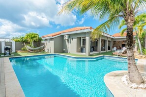 A swimming pool with a tiled edge, a hammock, and a palm tree. - Casa Karlina - Three Bedroom Villa, Sleeps 6 (Noord)