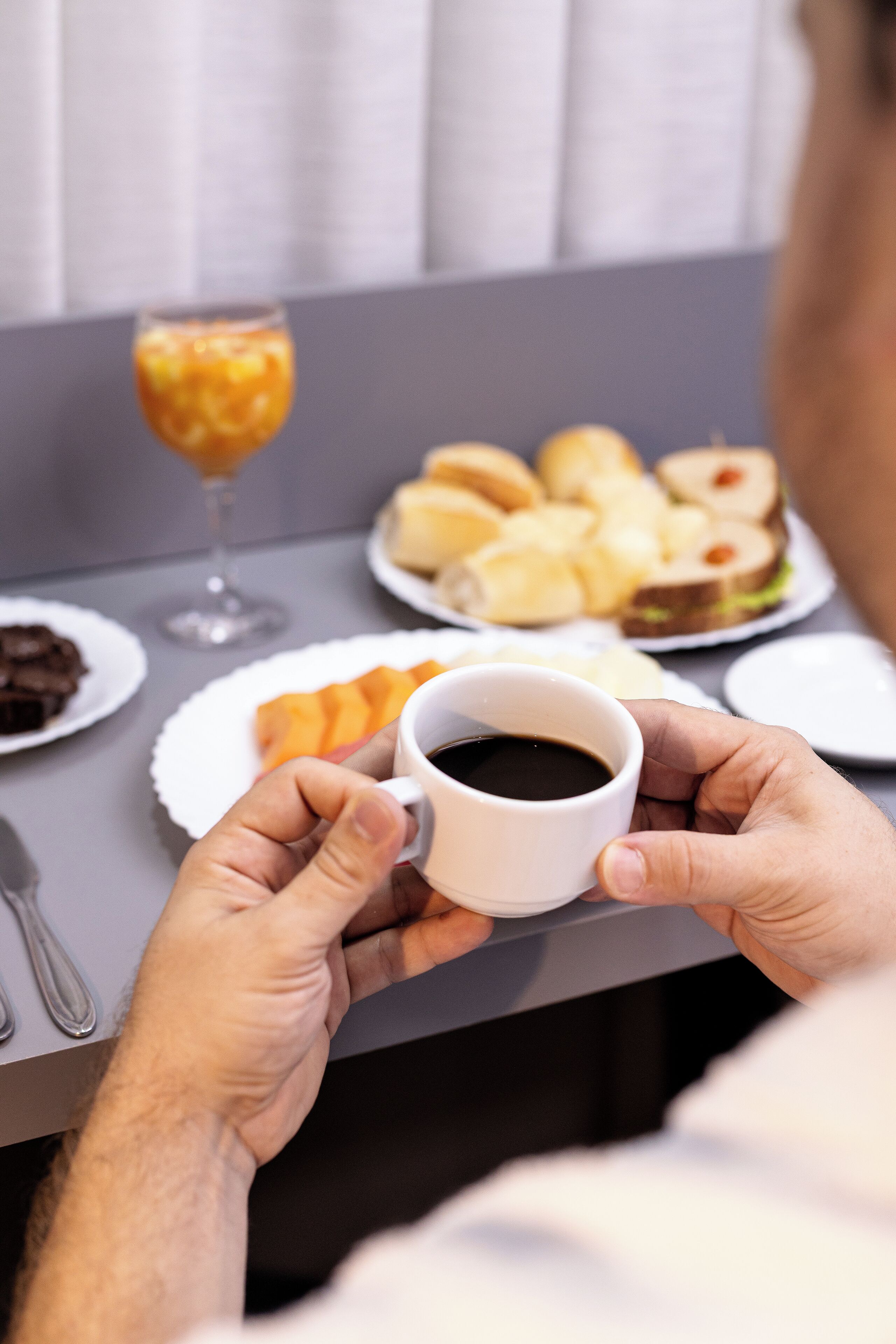A person holding a cup of coffee at a table with various food items and a glass of orange juice.