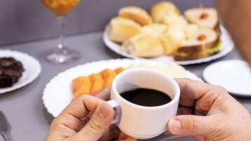 A person holding a cup of coffee at a table with various food items and a glass of orange juice.