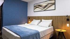 A neatly made bed with a blue blanket, a wooden headboard, and a wall-mounted abstract art piece. - Days Inn By Wyndham Cascavel (Cascavel)
