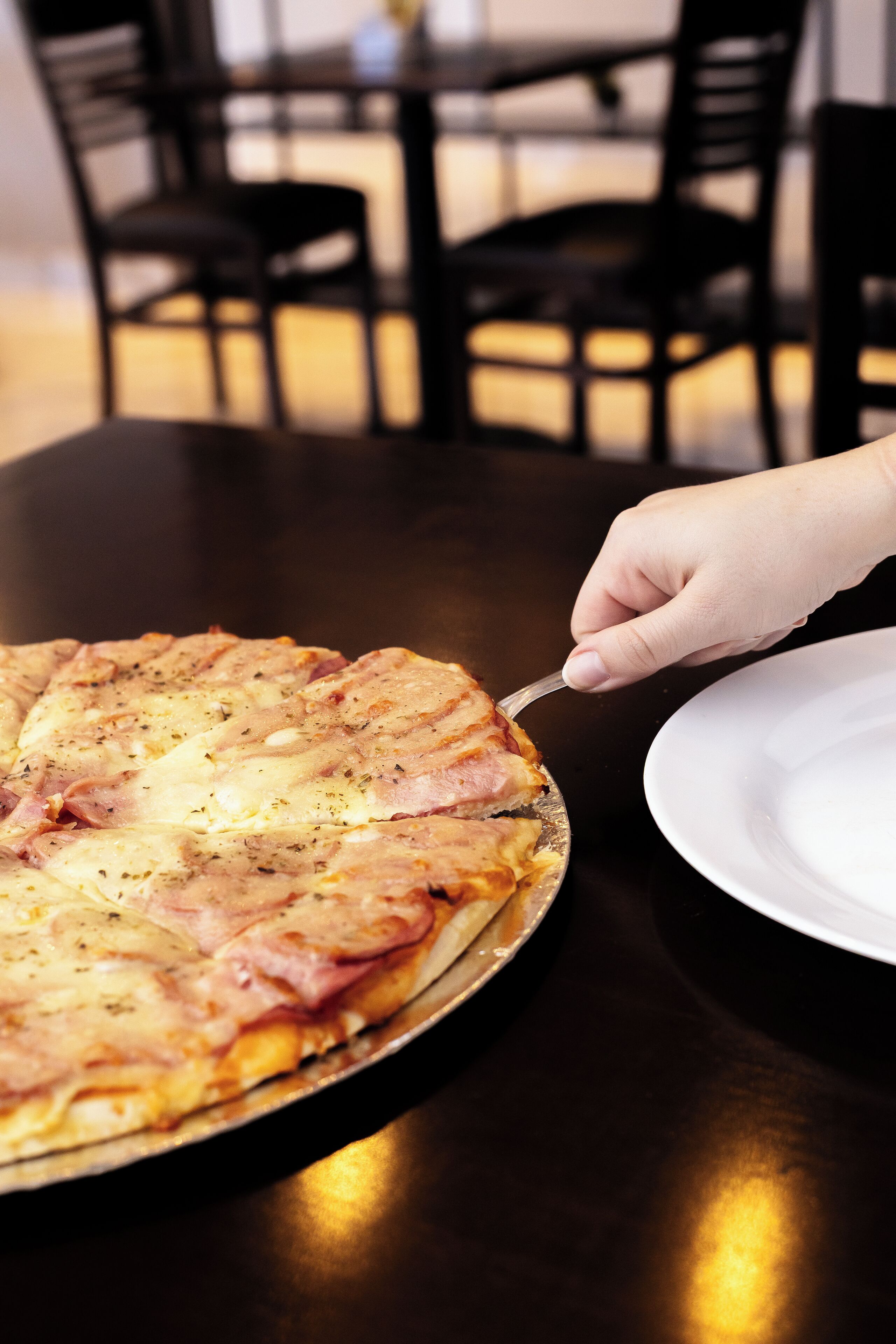 Una pizza sobre una mesa redonda, con una mano sosteniendo un cuchillo.