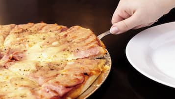 Una pizza sobre una mesa redonda, con una mano sosteniendo un cuchillo.