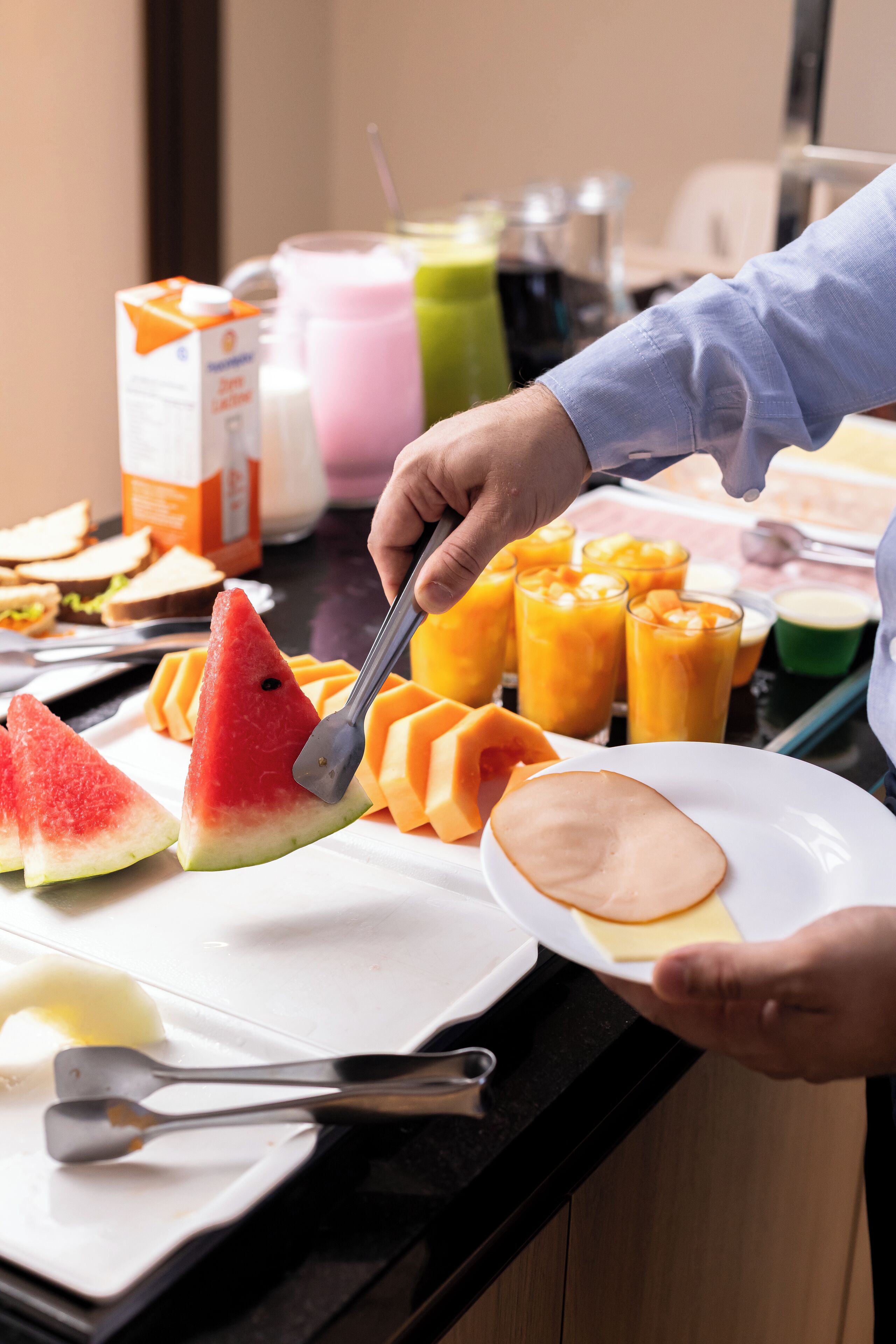 A breakfast buffet with various fruits, juices, and a carton of orange juice.